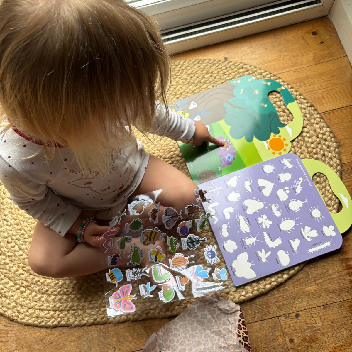 Child playing with sticker books on a wooden floor